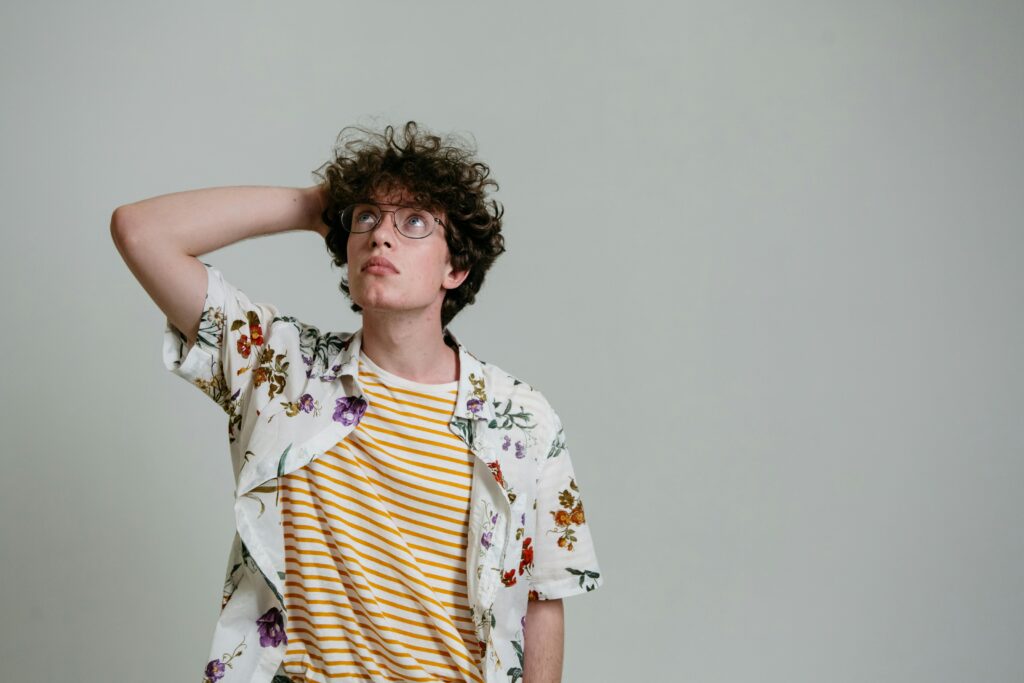 A young man with curly hair and glasses thinking in a studio setting.